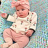 baby, infant, child, knitted_blanket, pink_bow, headband, sweater, floral_pattern, pink_pants, cozy, cute, soft_texture, pastel_colors, portrait, indoors, candid, small_hands, socks, seated, comfortable