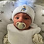 baby, pacifier, hat, pom_pom, bib, infant, sleeping_baby, star_pattern, cushion, blanket, cute, newborn, face, clothing, indoors, resting, soft_lighting, child, young, peaceful