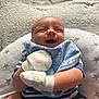baby, smiling, mittens, bib, blue_clothing, striped_clothing, cushion, star_pattern, happy, infant, cute, lying_down, soft_texture, child, newborn, portrait, comfortable, indoor, person, face