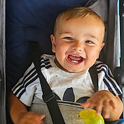 Logan is registered to the contest to win money with this photo: toddler, child, smiling, happy, stroller, toy, yellow_toy, white_shirt, navy_stripes, seatbelt, baby, infant, cute, joyful, portrait, face, hand, clothing, baby_toy, childhood