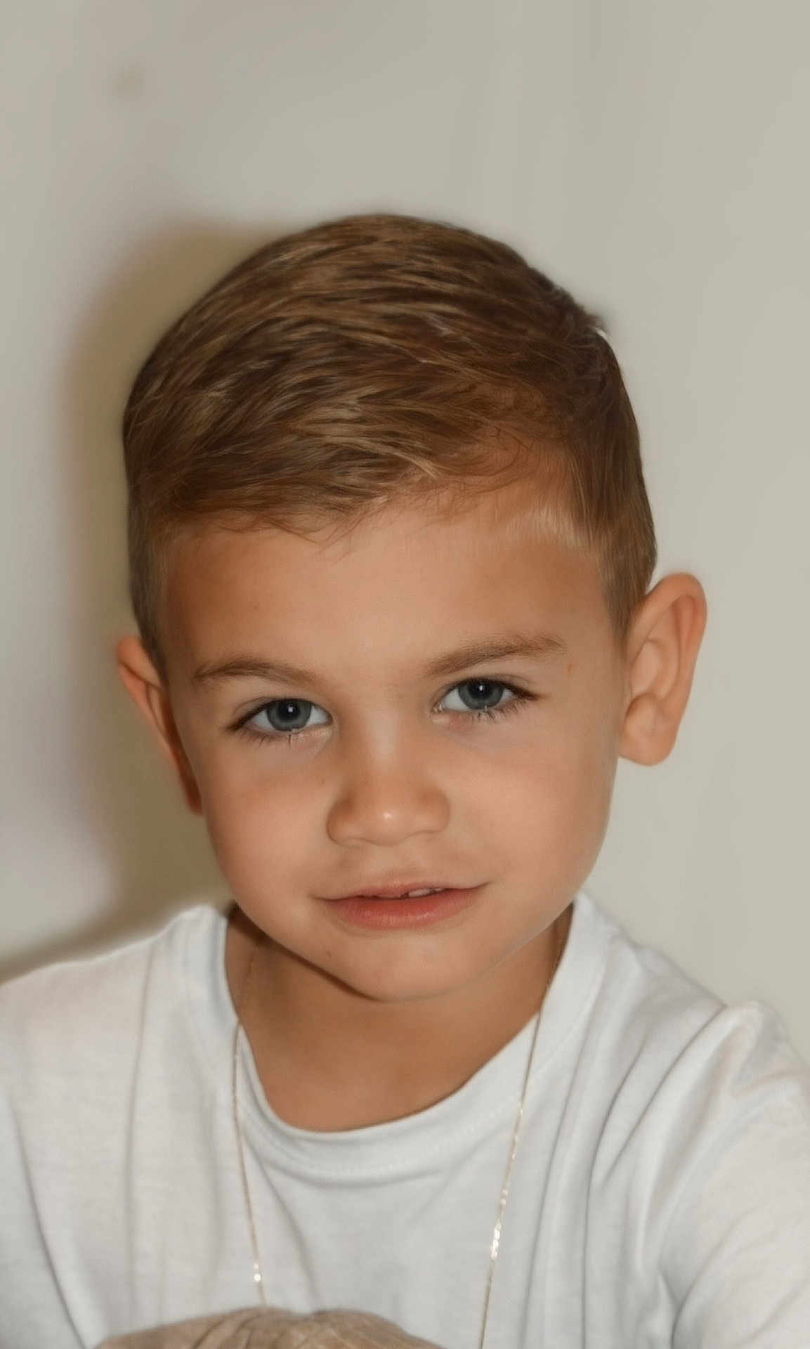 Elio participe au concours pour gagner de l'argent avec cette photo : child, boy, portrait, face, smile, white_shirt, necklace, short_hair, blue_eyes, close_up, innocent, cute, young, casual, neutral_background, human, person, head_and_shoulders, looking_at_camera, indoor