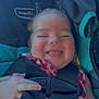 baby, child, smiling, car_seat, seatbelt, pigtails, red_clothing, checkered_pattern, happy, infant, cute, face, hand, straps, safety, child_seat, person, indoors, closeup, portrait