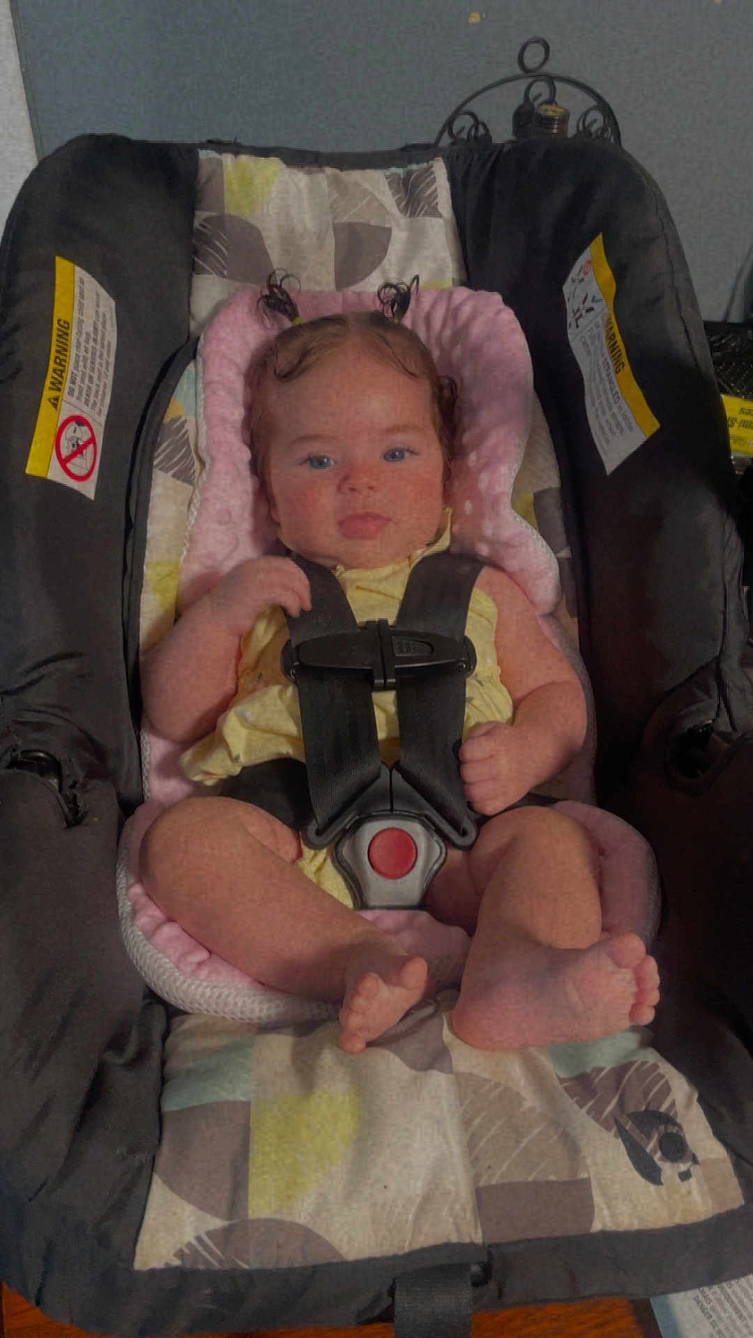 June joined the competition — help win amazing prizes! baby, car_seat, child, infant, harness, pink_cushion, patterned_blanket, indoor, face, person, cute, hair, pigtails, sitting, safety, seat, clothing, foot, hand, expression