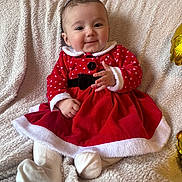 Inaya a rejoint le concours — aidez-le/la à gagner de superbes lots ! baby, child, smiling, red_dress, white_trim, sitting, blanket, indoors, cute, holiday_outfit, festive, cozy, portrait, happy, infant, clothing, soft_texture, face, person, warm