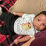 baby, child, infant, lying_down, blanket, red, black, clothing, tshirt, pants, person, face, hair, skin, cute, pattern, comfort, indoor, adult_arm, looking_away