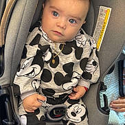 Dylan is registered to the contest to win money with this photo: baby, car_seat, mickey_mouse, clothing, child, infant, seatbelt, footwear, sitting, curious, blue_eyes, gold_chain, hand, gray, black_and_white, indoors, person, cute, portrait, casual