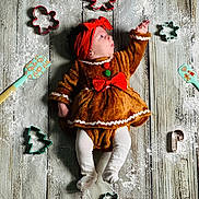 Elodie joined the competition — help win amazing prizes! baby, infant, gingerbread_costume, red_headband, cookie_cutters, flour, wooden_floor, holiday_theme, cute, child, white_tights, lying_down, decor, seasonal, festive, small_person, baking_tools, red_bow, playful, holiday_baby