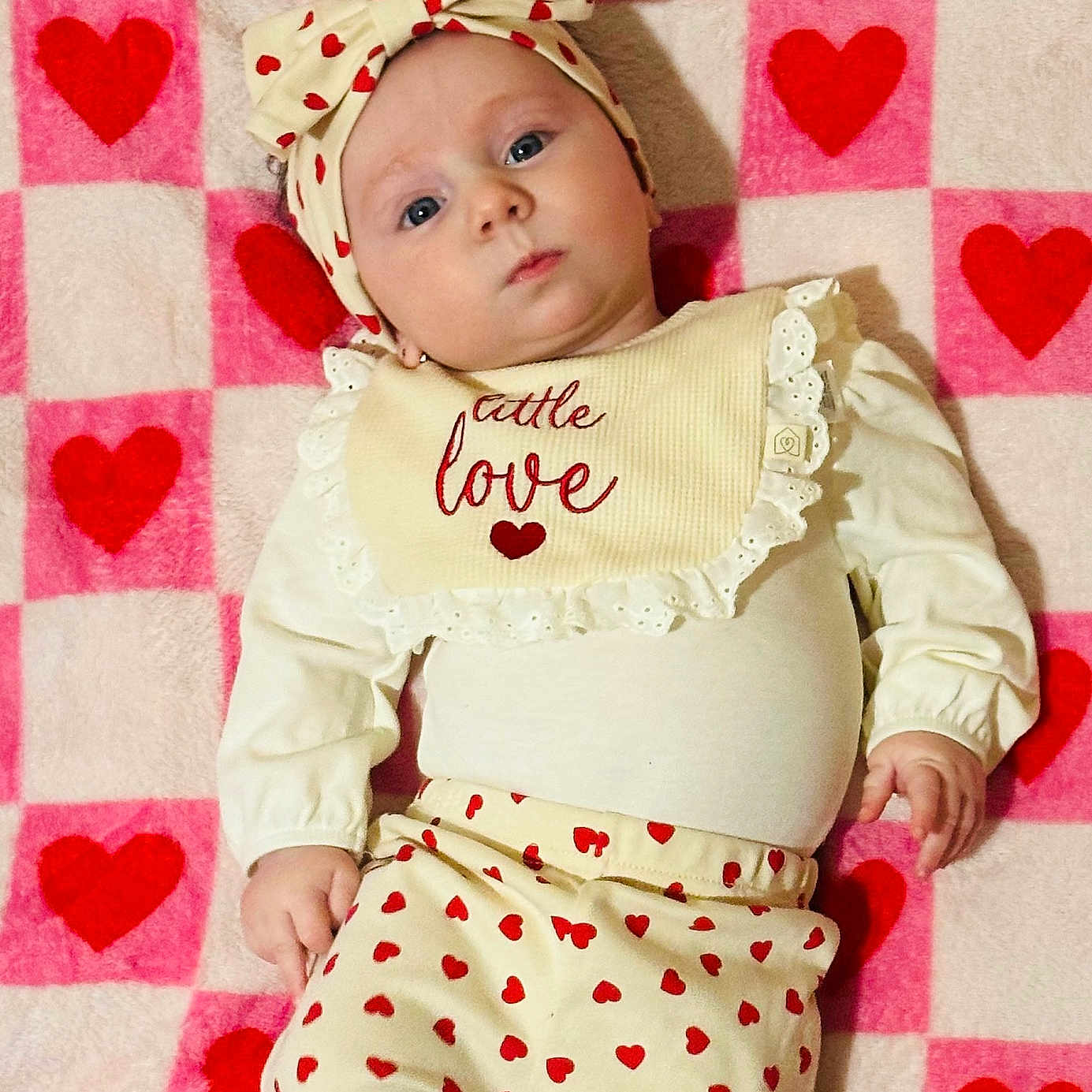 Elodie is registered to the contest to win money with this photo: baby, infant, heart_pattern, headband, blanket, pink, red, cute, clothing, portrait, lying_down, child, face, expression, soft_texture, warm_colors, patterned_pants, long_sleeve, adorable, love