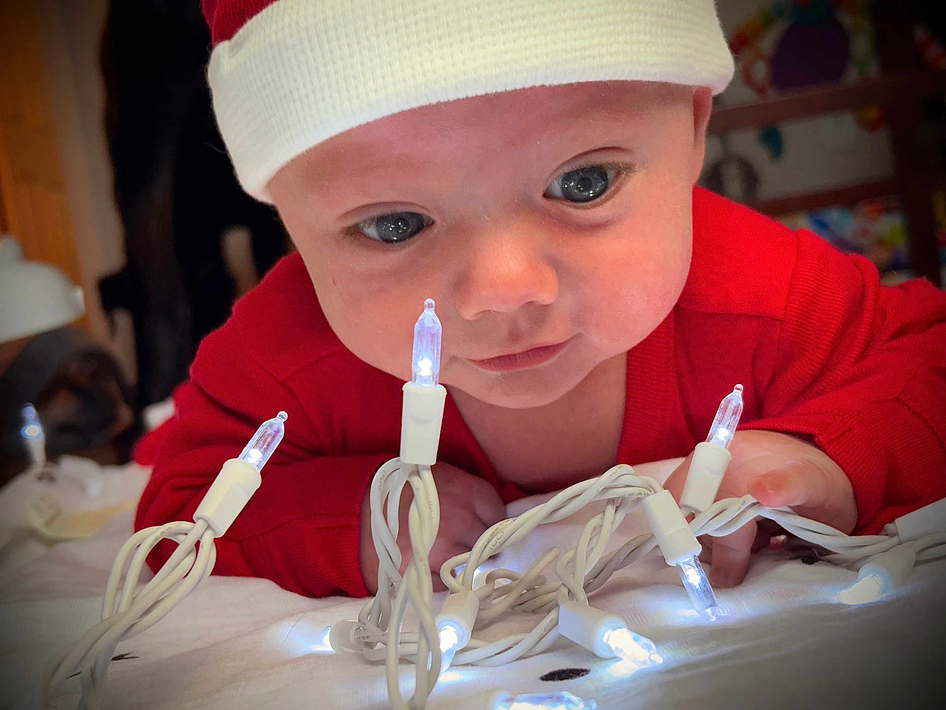 Rylin is registered to the contest to win money with this photo: baby, infant, face, eyes, christmas_lights, red_clothing, hat, holiday, indoors, curious, hands, close_up, white_lights, cute, child, toddler, festive, expression, portrait, exploration