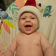 Lowen a rejoint le concours — aidez-le/la à gagner de superbes lots ! baby, infant, smiling, santa_hat, holiday, festive, child, happy, cute, portrait, patterned_background, colorful, indoors, seat, toy, wearing_hat, skin, person, expression, celebration