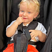 Taj is registered to the contest to win money with this photo: toddler, child, blonde_hair, blue_eyes, stroller, car_seat, orange_clothing, white_shirt, baby, sitting, cute, face, hand, safety_harness, infant, portrait, baby_clothes, young_child, baby_fashion, seat