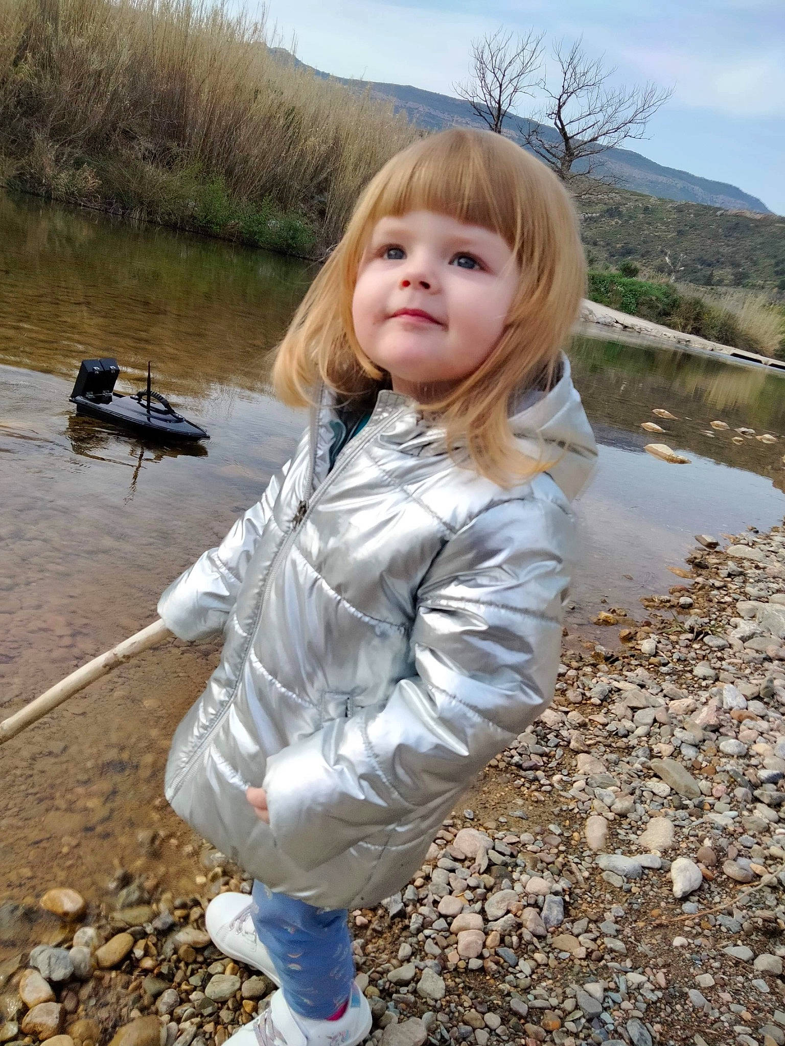 Inaya participe au concours pour gagner de l'argent avec cette photo : bank, blond, child, fun, grass, jacket, lake, landscape, leisure, nature, people_in_nature, person, sand, sitting, sky, soil, toddler, water, wilderness, winter