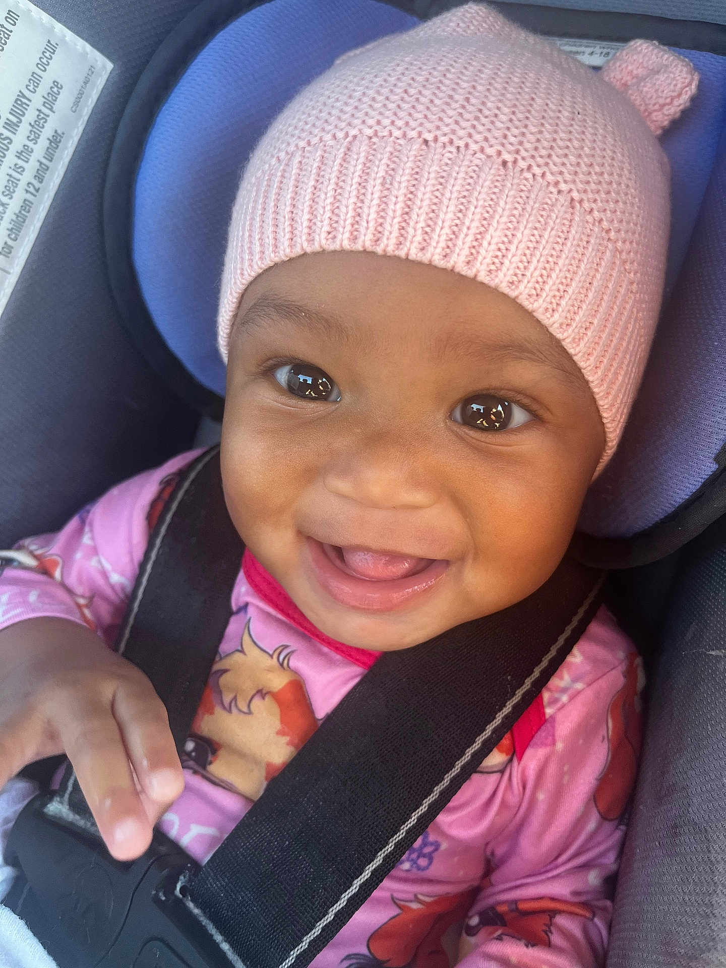 Aurelia is registered to the contest to win money with this photo: baby, child, car_seat, pink_hat, knit_hat, smiling, happy, infant, seatbelt, clothing, cute, portrait, close_up, young_child, baby_girl, car_interior, safety, face, expression, playful