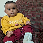 Sharavin is registered to the contest to win money with this photo: baby, child, yellow_sweatshirt, maroon_pants, striped_socks, couch, patterned_fabric, indoors, portrait, cute, sitting, small_ears, short_hair, expression, comfortable, furniture, clothing, person, young_child, casual
