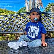 Amir joined the competition — help win amazing prizes! toddler, child, pacifier, blue_shirt, text_on_clothing, cap, backwards_cap, jeans, white_sneakers, bench, outdoor, sunny, sky, palm_trees, greenery, bracelet, chain_necklace, garden, portrait, casual