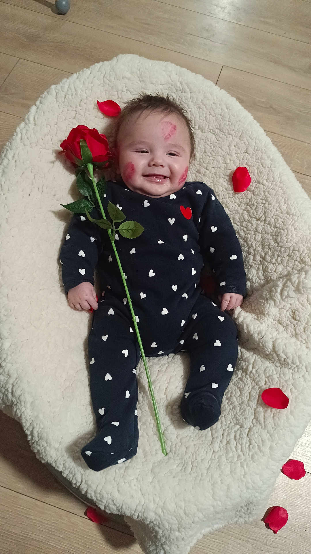 Timéo a rejoint le concours — aidez-le/la à gagner de superbes lots ! baby, infant, smiling, onesie, heart_pattern, rose, rose_petals, face_paint, fluffy_cushion, wooden_floor, cute, happy, lying_down, indoor, soft_texture, red, black_clothing, cheeks, head, person