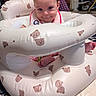 baby, infant, inflatable_seat, teddy_bear_pattern, smile, face, foot, indoor, carpet, person, cute, child, playful, pink_bib, clothing, human, head, sitting, expression, comfort