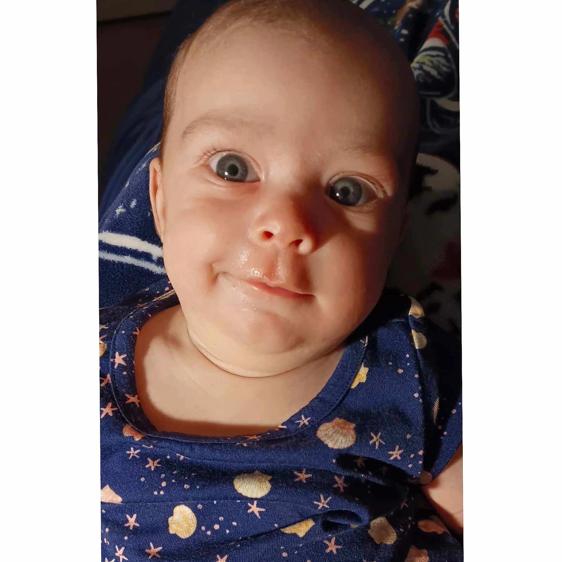 Aurora is registered to the contest to win money with this photo: baby, infant, face, eyes, smile, blue_clothing, stars, planets, pattern, portrait, closeup, skin, child, cute, young, head, person, apparel, baby_garment, expression