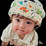 baby, child, helmet, padded_helmet, dinosaur_print, cute, infant, face, curious, clothing, white_shirt, portrait, closeup, headgear, black_background, looking_up, indoors, baby_face, child_portrait, adorable