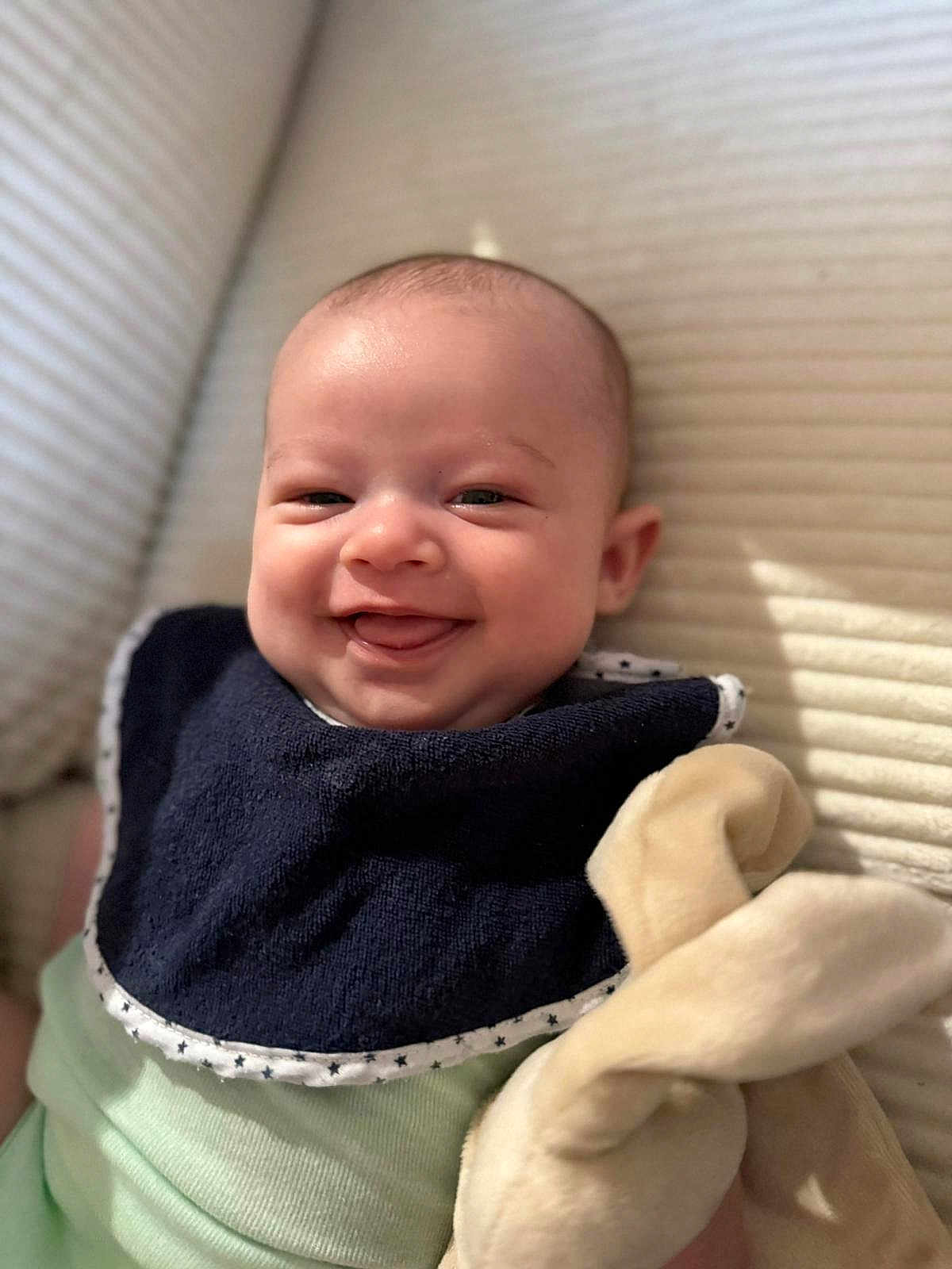 Timéo a rejoint le concours — aidez-le/la à gagner de superbes lots ! baby, smiling, bib, plush_toy, bunny_ears, cozy, soft_toys, infant, cute, portrait, happy, child, indoor, closeup, skin, clothing, lying_down, head, face, baby_bib