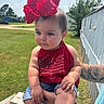 baby, child, red_bow, red_tank_top, blue_eyes, tattoo, arm, outdoor, grass, daylight, person, cute, summer_clothing, denim_shorts, wooden_rail, greenery, portrait, infant, casual, holding