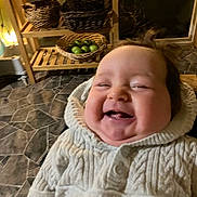 Amelia joined the competition — help win amazing prizes! baby, child, smiling, knitted_sweater, indoor, wooden_shelf, baskets, green_apples, floor_tiles, happy, face, portrait, cozy, cute, infant, warm_lighting, home, person, sitting, candid