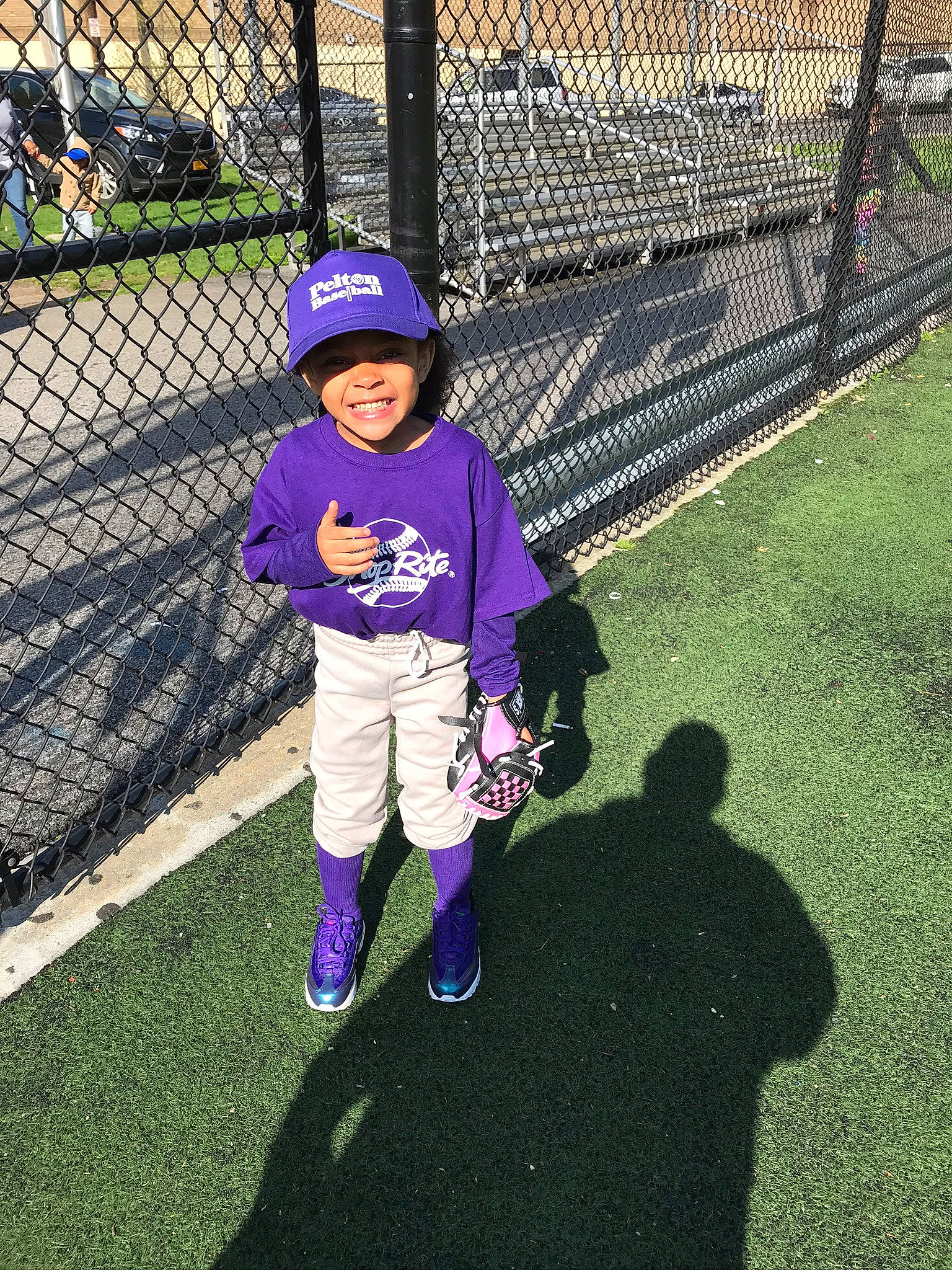 Janiyah joined the competition — help win amazing prizes! baby_toddler_clothing, baseball_player, electric_blue, fence, fun, grass, hat, headwear, helmet, joy, mesh, person, plant, player, purple, recreation, smile, sneakers, sports_equipment, sports_gear