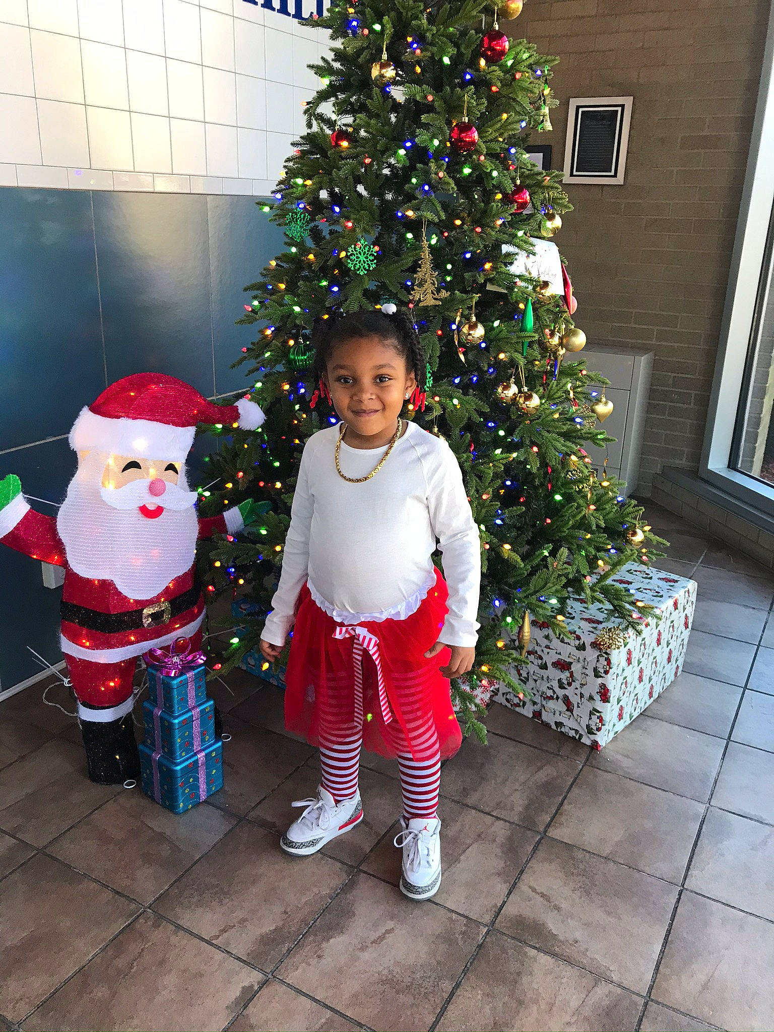 Janiyah is registered to the contest to win money with this photo: christmas, christmas_decoration, christmas_ornament, christmas_tree, event, evergreen, fun, green, holiday, holiday_ornament, joy, ornament, person, plant, red, santa_claus, standing, toddler, tree, white