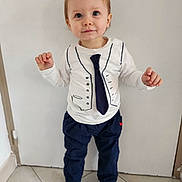 Alessio participe au concours pour gagner de l'argent avec cette photo : black_shoes, child, curious, cute, indoor, navy_pants, pants, person, plain_background, shirt, short_hair, smile, sneakers, standing, tie_print, tile_floor, toddler, vest_print, white_shirt, young_child