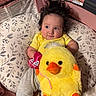 Anaya Rose is registered to the contest to win money with this photo: baby, child, plush_toy, yellow_shirt, gray_pants, pillow, patterned_pillow, stuffed_animal, duck, orange_beak, hand, curly_hair, indoor, cute, infant, lying_down, soft_toy, comfort, clothing, looking_away