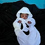 Aaron is registered to the contest to win money with this photo: baby, infant, newborn, ghost_costume, hood, white_fur, hands, bed, bedding, black_bedspread, blue_wall, portrait, cute, sleepy, indoors, one_child, costume, soft_texture, smile_design, relaxing