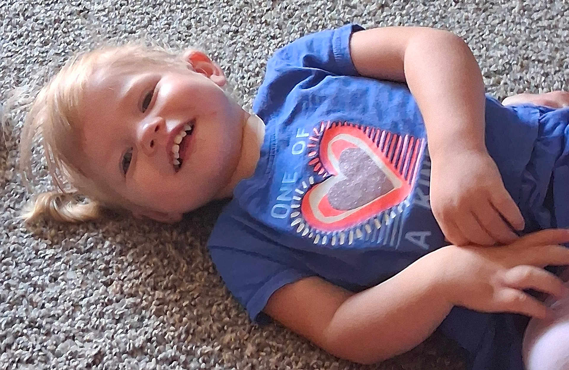 Nataila joined the competition — help win amazing prizes! child, toddler, smiling, blue_shirt, heart_print, carpet, lying_down, happy, cute, young_child, person, casual_clothing, indoor, small_hands, blond_hair, portrait, playing, relaxed, childhood, fun