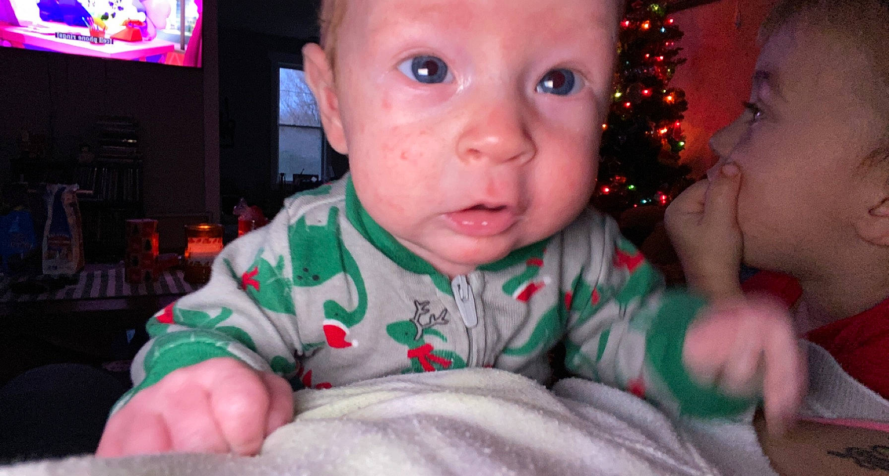 Atticus is registered to the contest to win money with this photo: baby, baby_toddler_clothing, cheek, chin, christmas_tree, eyebrow, facial_expression, finger, fun, happy, head, headwear, human_body, iris, lip, mouth, nose, organ, person, skin