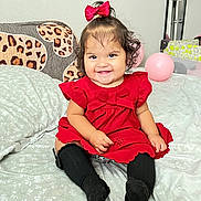 Khloe Mahiara is registered to the contest to win money with this photo: baby, child, smiling, red_dress, bow, black_socks, bed, pillow, balloon, indoor, cute, happy, portrait, sitting, curly_hair, drool, toddler, wall, blanket, infant