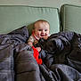baby, blanket, couch, plush_toy, smile, child, indoor, green_couch, gray_blanket, happy, portrait, infant, cozy, cute, person, furniture, home, comfort, young_child, soft_toys