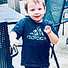 child, boy, smiling, outdoor, patio, chair, table, clothing, tshirt, camo, shorts, happy, person, furniture, playful, young, casual, daylight, portrait, motion