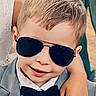 Oakley is registered to the contest to win money with this photo: child, boy, sunglasses, suit, bow_tie, smile, short_hair, badge, sheriff_badge, formal_wear, portrait, person, hand, adult_arm, fashion, cool, confident, indoor, closeup, face
