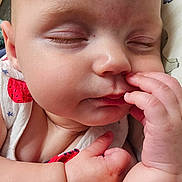 Stella is registered to the contest to win money with this photo: baby, infant, face, hand, sleeping, close_up, skin, arm, fingers, clothing, patterned_clothing, indoors, carpet, peaceful, cute, resting, person, child, newborn, portrait