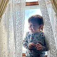 Ryker joined the competition — help win amazing prizes! toddler, child, window, curtains, lace, smile, mickey_mouse, sweater, indoors, natural_light, portrait, happy, cute, playful, clothing, person, young_child, home, cozy, bright