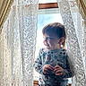toddler, child, window, curtains, lace, smile, mickey_mouse, sweater, indoors, natural_light, portrait, happy, cute, playful, clothing, person, young_child, home, cozy, bright