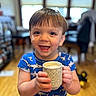 Ryker is registered to the contest to win money with this photo: toddler, child, smiling, blue_shirt, shark_pattern, mug, indoor, wooden_floor, happy, holding, drink, face, eyes, short_hair, person, young_child, furniture, background, window, light