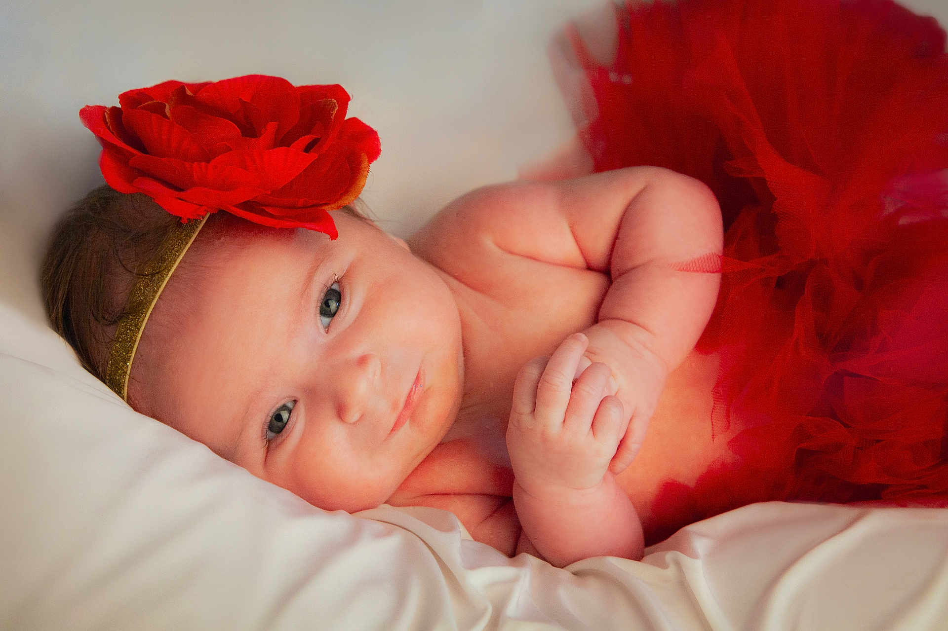 Abygaïl a rejoint le concours — aidez-le/la à gagner de superbes lots ! baby, infant, red_flower, headband, tutu, red_clothing, soft_pillow, lying_down, cute, smiling, portrait, skin, hand, face, newborn, child, indoors, closeup, sleepwear, adorable