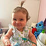 toddler, child, smile, face, hair, topknot, dress, toy, stuffed_animal, nursery, hand, bottle, room, cute, baby, happy, indoor, person, playful, infant