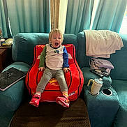 Arthur joined the competition — help win amazing prizes! toddler, child, red_chair, car_shaped_chair, living_room, couch, curtains, laptop, remote_control, purse, drink_cup, blanket, socks, sneakers, wooden_beam, carpet, person, indoor, expression, furniture