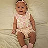 baby, child, infant, smiling, sitting, portrait, bed, bedroom, headband, bow, floral_outfit, pink_socks, clothing, barefoot, happy, cute, indoor, soft_lighting, bedding, photograph