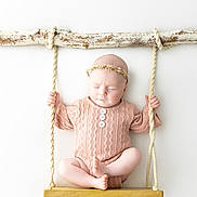 Lottie is registered to the contest to win money with this photo: baby, infant, swing, wood, rope, headband, pink_clothing, closed_eyes, peaceful, cute, portrait, studio, knitwear, soft_lighting, minimalist, white_background, child, newborn, sitting, decorative