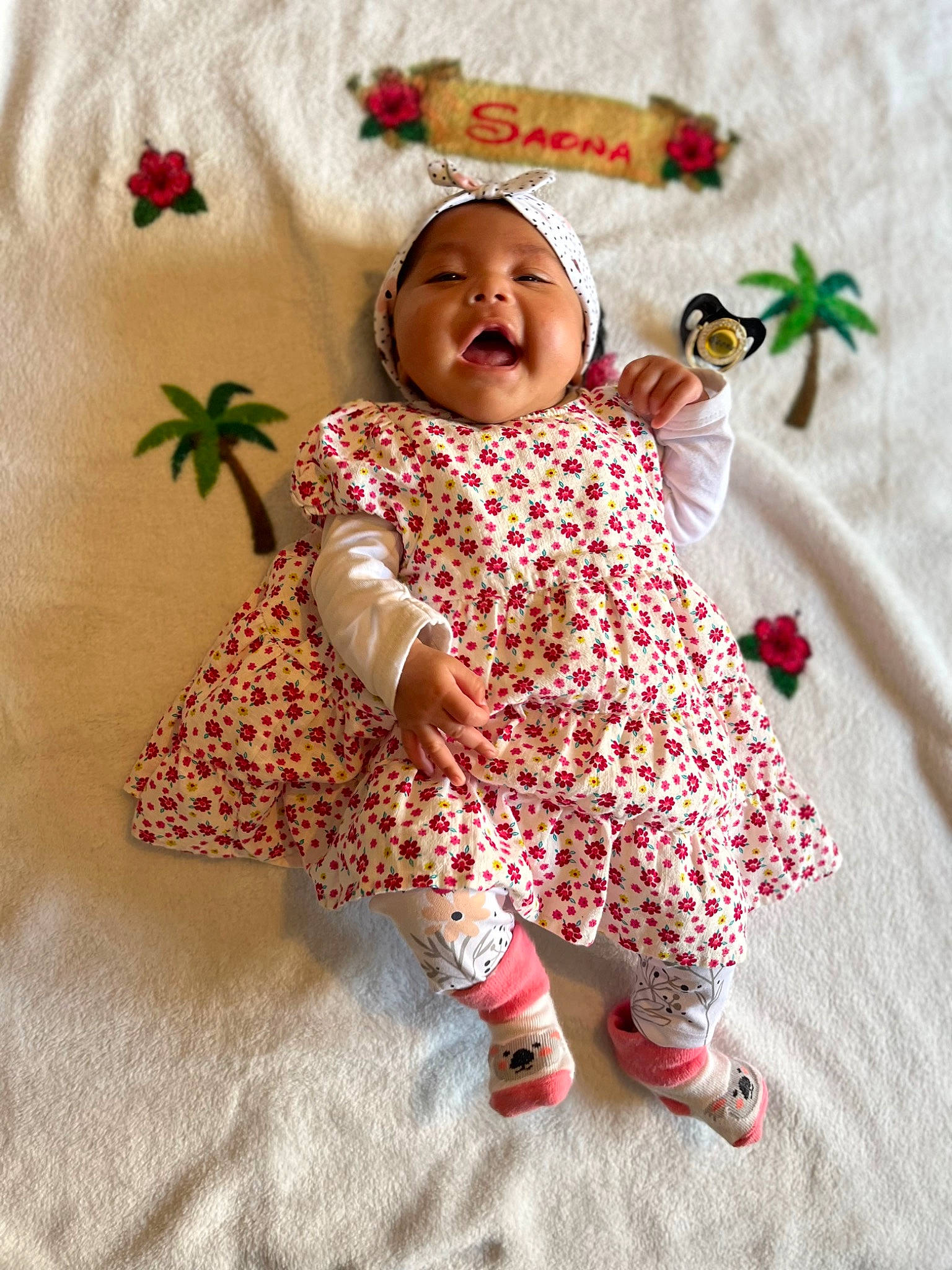 Saona participe au concours pour gagner de l'argent avec cette photo : baby, baby_toddler_clothing, child, dress, face, happy, head, headwear, linens, magenta, outerwear, pattern, peach, person, pink, room, sitting, skin, sleeve, smile