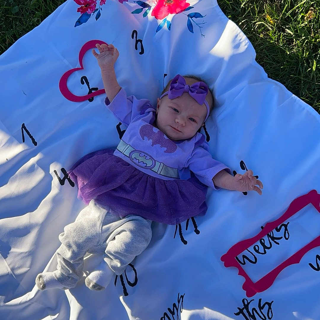 Raelynn joined the competition — help win amazing prizes! baby, blanket, clothing, dress, face, furniture, grass, hat, head, nature, outdoors, park, people, person, photography, plant, portrait, purple, quilt, text