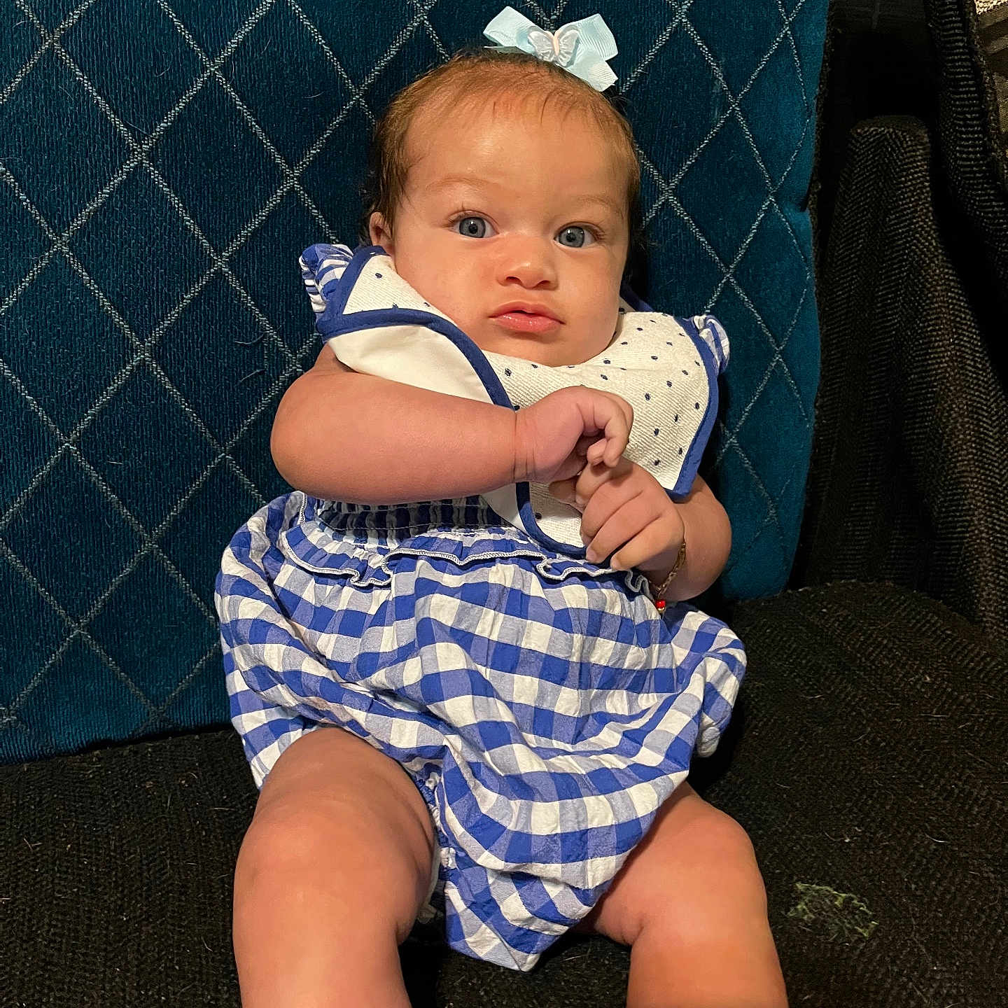Nirahylez is registered to the contest to win money with this photo: baby, blue_dress, bow, checkered_pattern, child, clothing, cute, cute_face, expression, fabric, headwear, indoor, infant, person, portrait, quilted_background, sitting, skin, small_hands, young