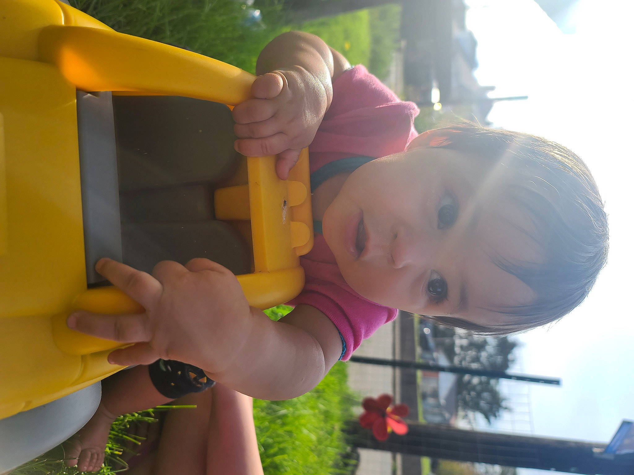 Hazel is registered to the contest to win money with this photo: arm, child, facial_expression, finger, fun, gesture, grass, hand, happy, leisure, outdoor_play_equipment, person, plant, public_space, recreation, smile, surprise, tire, toddler, tree